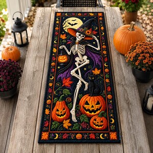 May include: A rectangular table runner featuring a black background with a central skeleton wearing a witch hat and cape, holding a jack-o'-lantern. The design includes a black cat, multiple orange pumpkins, colourful autumn leaves, and a full moon.