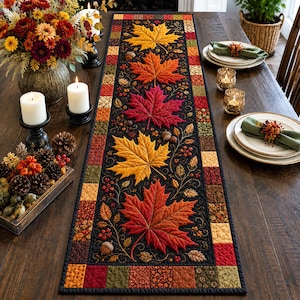 Può includere: Un runner da tavola trapuntato rettangolare con un pannello centrale nero decorato con grandi foglie d'acero ricamate nei toni del giallo, arancione e rosso, circondato da un bordo di piccoli quadrati di tessuto multicolore autunnali.