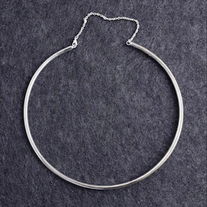 May include: A silver-toned metal choker necklace featuring a rigid, circular band that forms the main body of the piece. The two ends of the circular band are connected by a delicate, thin silver-toned chain that includes a small lobster claw clasp.