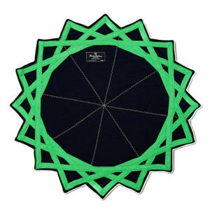 Op de afbeelding: Een ronde zwarte stoffen mat met een levendig groen geometrisch sterpatroon op het oppervlak. Het ontwerp bestaat uit elkaar kruisende lijnen die een twaalfpuntige stervorm vormen. Een klein rechthoekig label bevat de tekst Hewchakra.