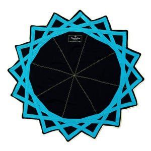 Op de afbeelding: Een ronde zwarte stoffen mat met een geometrisch sterpatroon in helder turkooisblauw. Het ontwerp bestaat uit overlappende lijnen die vanuit het midden uitstralen, geaccentueerd met gele zigzagstiksels en een centraal Hexchakra-label.