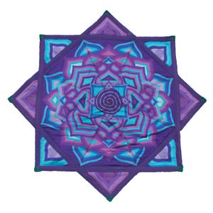 Puede incluir: Una alfombrilla de tela cuadrada con un diseño de mandala en capas en tonos púrpura, violeta y cian brillante. El centro muestra un motivo en espiral, rodeado de pétalos geométricos simétricos y esquinas triangulares con espirales.