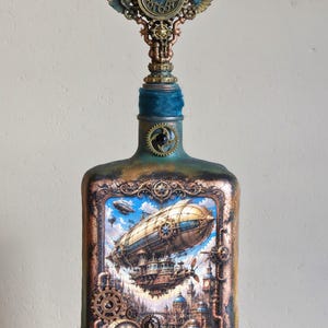 Könnte beinhalten: Eine dekorative Glasflasche mit einer detaillierten Illustration eines Luftschiffs und einer Stadtlandschaft. Der Flaschenhals ist mit blauem Samt umwickelt und mit einer geflügelten Metalluhr gekrönt. Die Oberfläche ist mit Bronzezahnrädern verziert.