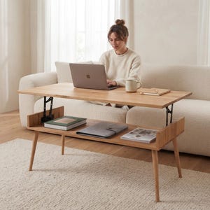 May include: A light-toned wooden coffee table featuring a lift-top mechanism that elevates the surface. The table has four tapered legs and an open lower storage shelf containing three books. The rectangular top is currently in the raised position.