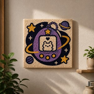 May include: A square punch needle wall hanging featuring a purple digital pet device with a screen displaying a small creature and a heart. The design includes yellow stars, a purple planet with a yellow ring, and a dark blue background on a cream base.