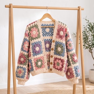 May include: A long-sleeve crochet cardigan featuring a patchwork of square motifs with floral patterns in shades of dusty pink, sage green, light blue, and cream. The garment has a V-neckline, a button-front closure with five brown buttons, and ribbed cuffs.
