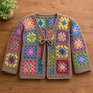 May include: A long-sleeved cardigan made from brown yarn, featuring a patchwork of multi-colored granny squares in shades of pink, yellow, blue, green, and purple. The front opening includes two brown crocheted ties with tassels at the ends.