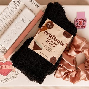 May include: A gift set containing a white reading list notepad, a white Gritin book light, a pink pen, black fuzzy socks, a Craftmix Espresso Martini drink packet, a pink satin scrunchie, and two stickers with text including Smutty Book Club.