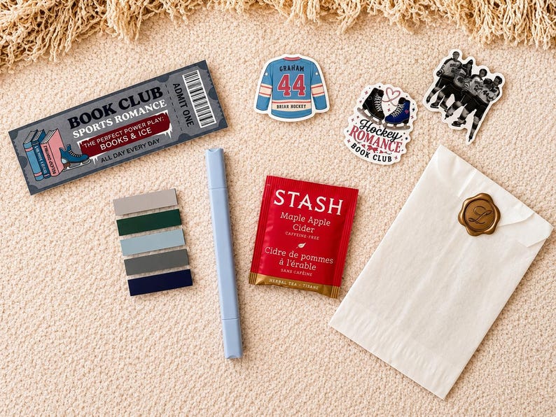 May include: A collection of items including a rectangular ticket reading Book Club Sports Romance, three stickers featuring a hockey jersey, skates, and players, a light blue marker, a set of five colored page flags, a Stash tea bag, and a white envelope.