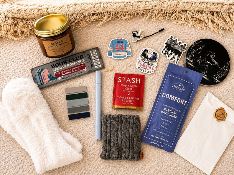 May include: A gift set including a Cedar & Sandalwood candle, a Book Club Sports Romance bookmark, a blue hockey jersey sticker, a Hockey Romance sticker, a Stash Maple Apple Cider tea bag, Comfort mineral bath soak, and white fuzzy socks.