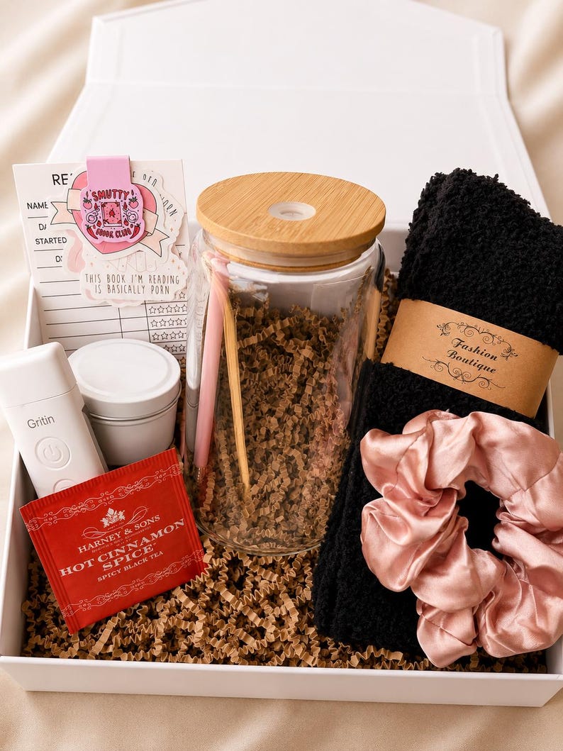 May include: A gift box containing a glass tumbler with a bamboo lid, a pink pen, a white Gritin device, a Harney & Sons Hot Cinnamon Spice tea packet, a black fuzzy pair of socks with a Fashion Boutique label, and a pink satin scrunchie.