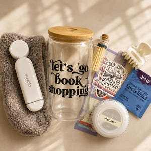 May include: A gift set containing a fuzzy brown sock, a white Vavolo device, a clear glass tumbler with a bamboo lid and the black text "let's go book shopping", a small glass vial of matches, a sticker, a white hair claw, and a Yogi tea bag.