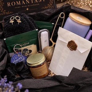 May include: A gift box containing a pair of gold dragon hoop earrings, a black velvet scrunchie, a green tea packet, a white electric lighter, a gold tea infuser, a candle labelled Cedarwood & Balsam, and a white paper bag with a wax seal.