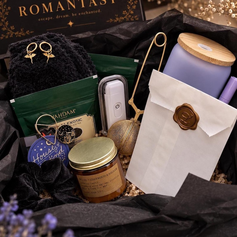 May include: A gift box containing a pair of gold dragon hoop earrings, a black velvet scrunchie, a green tea packet, a white electric lighter, a gold tea infuser, a candle labelled Cedarwood & Balsam, and a white paper bag with a wax seal.