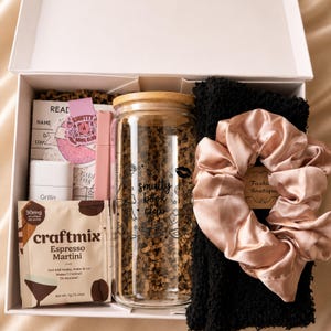 May include: A white gift box containing a glass tumbler with a bamboo lid and the text 'smutty book club', a packet of Craftmix Espresso Martini, a pink pen, a reading log card, a black textured fabric item, and a pale pink satin scrunchie.