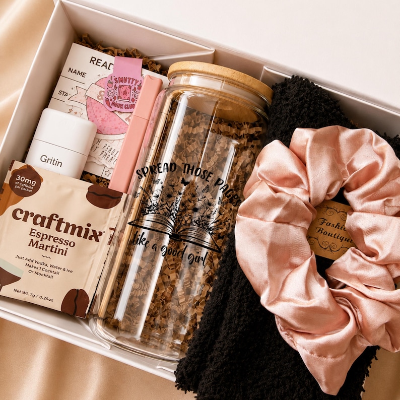 May include: A gift box containing a glass tumbler with a bamboo lid and the text 'SPREAD THOSE PAGES like a good girl', a packet of Craftmix Espresso Martini, a white Gritin box, a pink pen, a reading log, and a pale pink satin scrunchie on a black fabric.