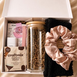 May include: A white gift box containing a clear glass tumbler with a bamboo lid, a black textured fabric item, a pink satin scrunchie, a Craftmix Espresso Martini drink packet, a white Gritin container, and a pink Smutty Book Club card.