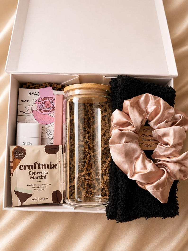 May include: A white gift box containing a clear glass tumbler with a bamboo lid, a black textured fabric item, a pink satin scrunchie, a Craftmix Espresso Martini drink packet, a white Gritin container, and a pink Smutty Book Club card.