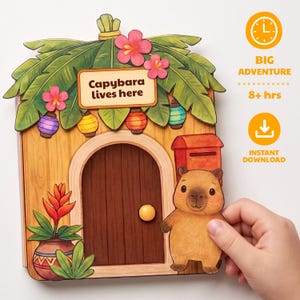Op de afbeelding: Een papieren knutselset met een huis in houtstijl en een bordje met de tekst Capybara lives here, versierd met palmbladeren, roze bloemen en lantaarns. Een uitgeknipte capybara-figuur staat naast de deur met een rode brievenbus.