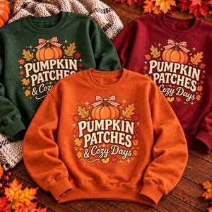 May include: Three crewneck sweatshirts in dark green, maroon, and orange. Each features a central graphic of a pumpkin with a plaid bow, surrounded by autumn leaves and the text "PUMPKIN PATCHES & Cozy Days" in a decorative font.