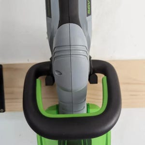 Può includere: Un tagliasiepi a batteria con corpo in plastica grigia e nera, un'impugnatura nera a forma di D e una protezione in plastica verde traslucida. Sul lato dell'utensile è chiaramente visibile la scritta 56V LITHIUM-ION in caratteri verdi.