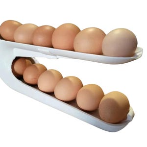 May include: A white plastic egg dispenser with a curved, two-tiered design. The rack holds twelve brown eggs, with six eggs arranged on the top shelf and six eggs positioned on the bottom shelf, creating a stacked, gravity-fed storage system.