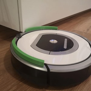 May include: A circular robotic vacuum cleaner with a white top surface, a black center panel featuring a central button labeled CLEAN, and a dark gray base. The device is equipped with a bright green curved bumper guard attached to the front edge.
