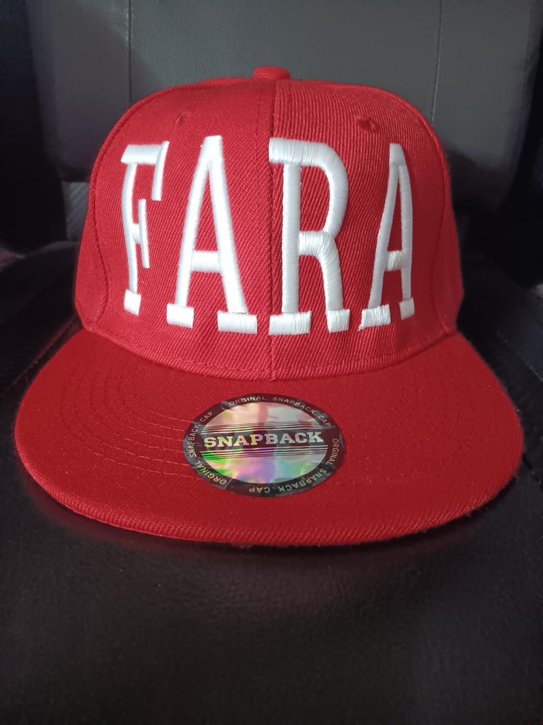 Pu&ograve; includere: Cappellino snapback rosso con la scritta "FARA" ricamata in bianco sul davanti. Il cappellino ha una visiera piatta e un adesivo "SNAPBACK".