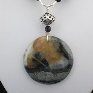 May include: A silver chain necklace with black beads and a silver pendant featuring a round, multi-colored stone with black and white accents.