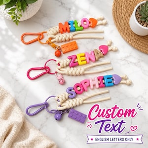 Peut inclure: Trois porte-clés en macramé avec une corde couleur crème, ornés de perles lettres en plastique coloré formant les prénoms MILO, ZENA et SOPHIE. Chaque porte-clés comprend un mousqueton assorti, une petite clochette et une breloque en brique.