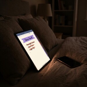 May include: A tablet displaying a digital note titled Ideas Vault with a purple banner and a list containing Moonlight Garden, Silent Disco, and Coffee App, positioned next to a smartphone on a textured surface in a dimly lit environment.