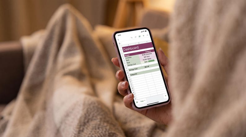 May include: A smartphone displaying a digital budget dashboard on its screen. The interface features a header labeled Dashboard, with rows for categories like Groceries, Rent, and Savings Goal, alongside numerical data and progress bars in shades of green.