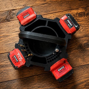 May include: A black plastic power tool battery charging station with a central handle and four red Hilti B22 2.6 lithium-ion batteries attached to the perimeter. The unit features a circular centre compartment and small holes for drill bits.