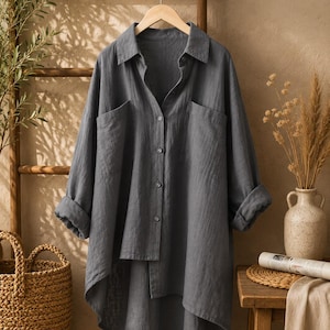 May include: A charcoal gray long-sleeve button-down shirt featuring a classic collar, two large chest pockets, and a high-low hemline. The shirt is displayed on a wooden hanger and has a textured fabric appearance with cuffed sleeves.