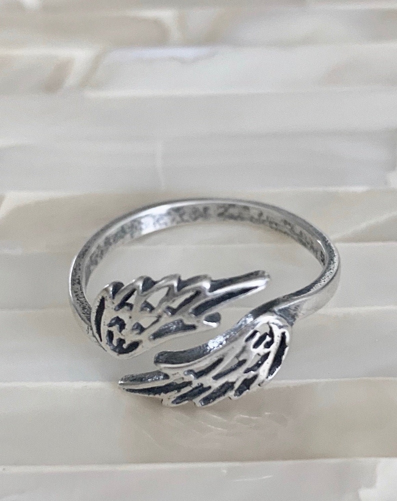 Op de afbeelding: Een zilveren ring met een ontwerp van twee open engelenvleugels. De ring is verstelbaar.