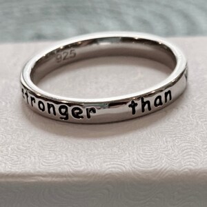 May include: A silver ring with the inscription "stronger than" engraved on the band.