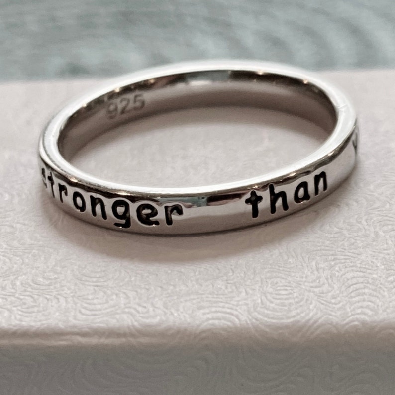 May include: A silver ring with the inscription "stronger than" engraved on the band.