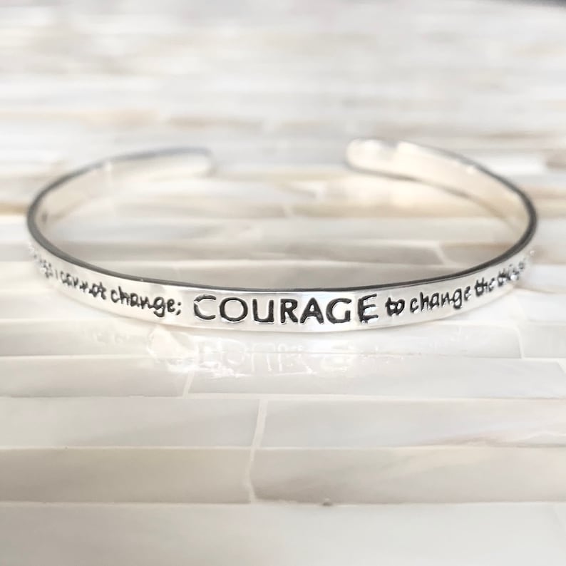 May include: Silver bangle bracelet with the inscription "You cannot change; COURAGE to change the things you cannot change."