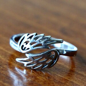 Op de afbeelding: Een zilveren ring met een ontwerp van twee open vleugels. De vleugels zijn aan de basis verbonden en de ring is verstelbaar.