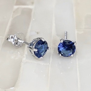 May include: A pair of silver stud earrings with a round, dark blue gemstone in each.