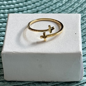 May include: A gold-toned ring with two small crosses that are intertwined. The ring is on a white background.