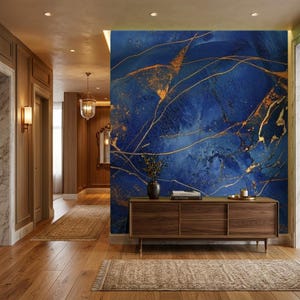 Può includere: Un murale con un motivo astratto in marmo blu intenso con venature dorate fluide. Il murale è installato su una parete dietro una lunga credenza rettangolare in legno con tre ante, un piccolo vaso e una pila di libri.