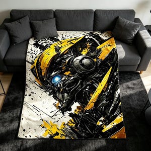 Puede incluir: Una manta rectangular con un gráfico abstracto de alto contraste de un personaje robótico en amarillo, negro y blanco. El diseño incluye detalles mecánicos, formas angulares nítidas y un ojo azul brillante sobre un fondo con salpicaduras de pintura.