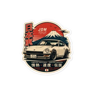 Puede incluir: Una pegatina troquelada que muestra un coche deportivo vintage blanco frente a un sol rojo y el monte Fuji. El diseño incluye texto en japonés, las palabras JDM y la frase Timeless Machines Endless Passion con una pequeña bandera japonesa.