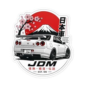 Puede incluir: Una pegatina de un coche deportivo Nissan Skyline GT-R blanco con un sol rojo, el monte Fuji y flores de cerezo. El diseño incluye el texto JDM, caracteres japoneses y la frase Japanese Passion Timeless Culture con un símbolo de infinito.