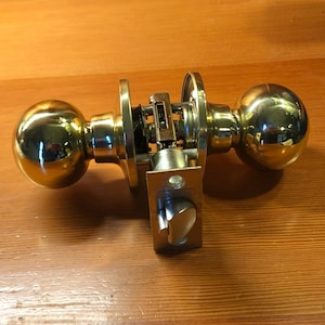 May include: A brass door knob with a round handle and a square latch. The knob is polished and shiny.