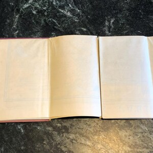 May include: A closed book with a pink cover and blank pages. The book is open to reveal the blank pages.