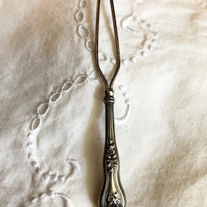 May include: A silver-toned, ornate, decorative hook with a floral design on the handle. The hook is designed to be used for hanging items.