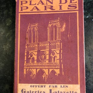 May include: A vintage red and orange paper booklet with the title "Plan de Paris" and the text "Offert par les Galeries Lafayette". The cover features a black and white illustration of the Notre Dame Cathedral.