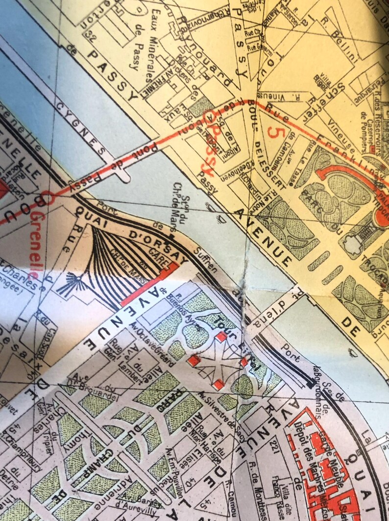 May include: A vintage map of Paris, France, showing the Seine River, the Eiffel Tower, and the Champs-Elysees. The map is printed on a yellowed paper with red and black lines.